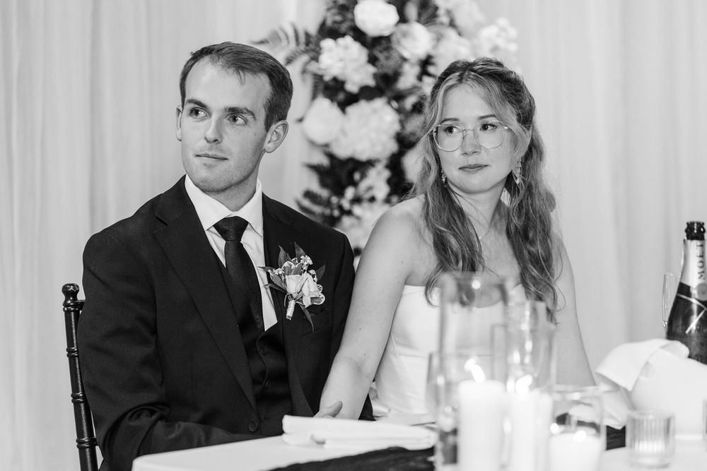 Bride and groom seated at wedding reception table in elegant black and white photo.