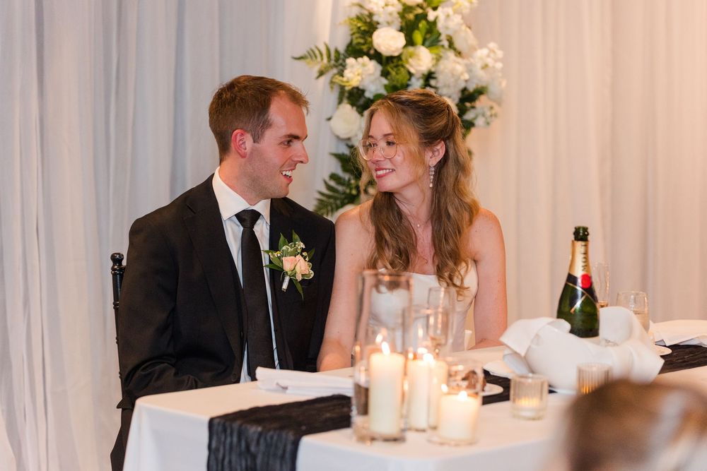 Smiling bride and groom share a joyful moment at their wedding reception table with candles and flowers.