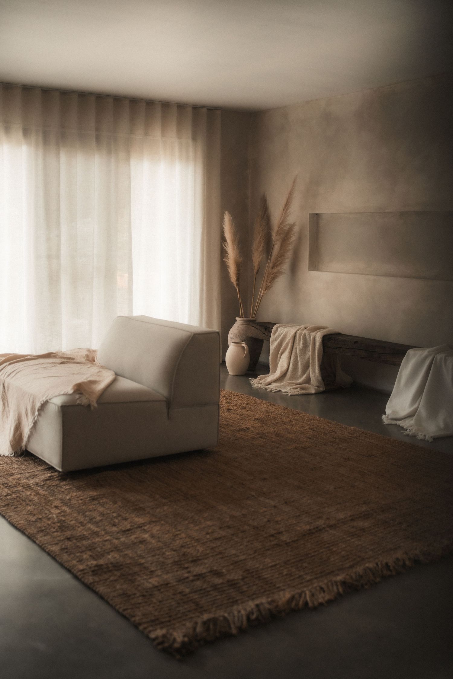 Cozy neutral living room with a cream sofa, woven jute rug, pampas grass in a vase, and sheer curtains softening the natural light.