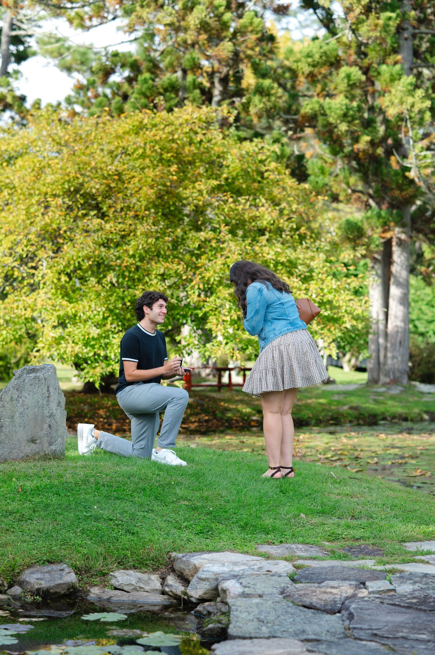 Man kneeling on one knee proposing to woman in the Japanese Stroll Gardens in North Salem, NY on a sunny September day.
