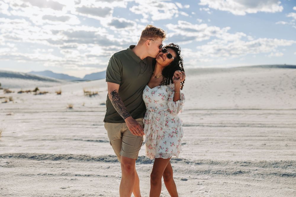 A couple shares a romantic moment in a white sand desert landscape under a cloudy sky.