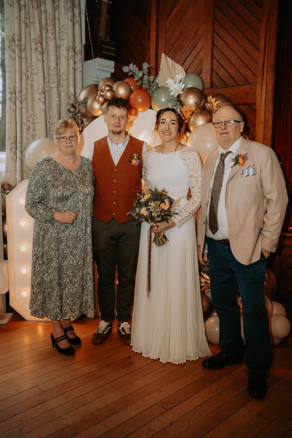 Wedding couple poses with family in front of balloon arch decor.