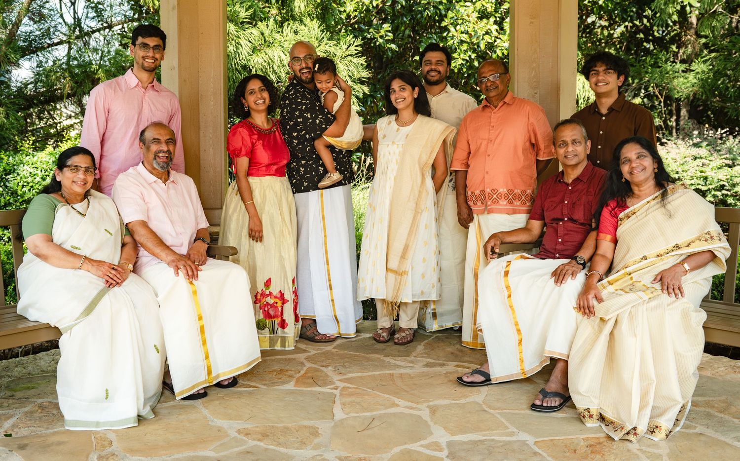 Large South Asian family in traditional white Kerala attire posing together outdoors under a garden pavilion in Atlanta for Portrait