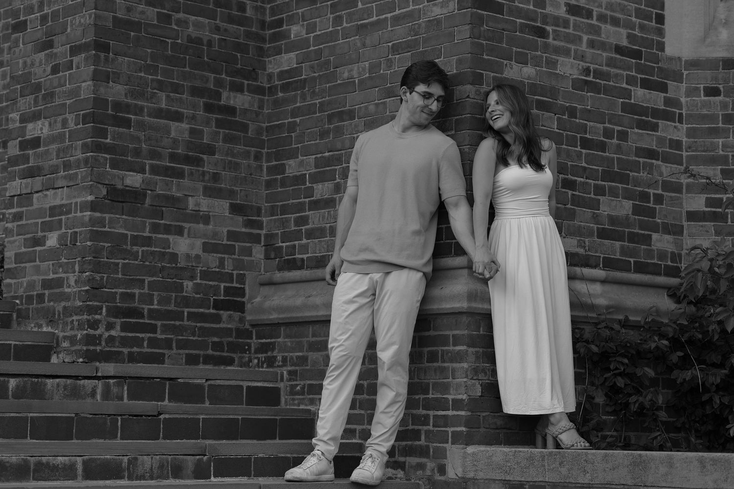 Couple holding hands leaning against brick wall