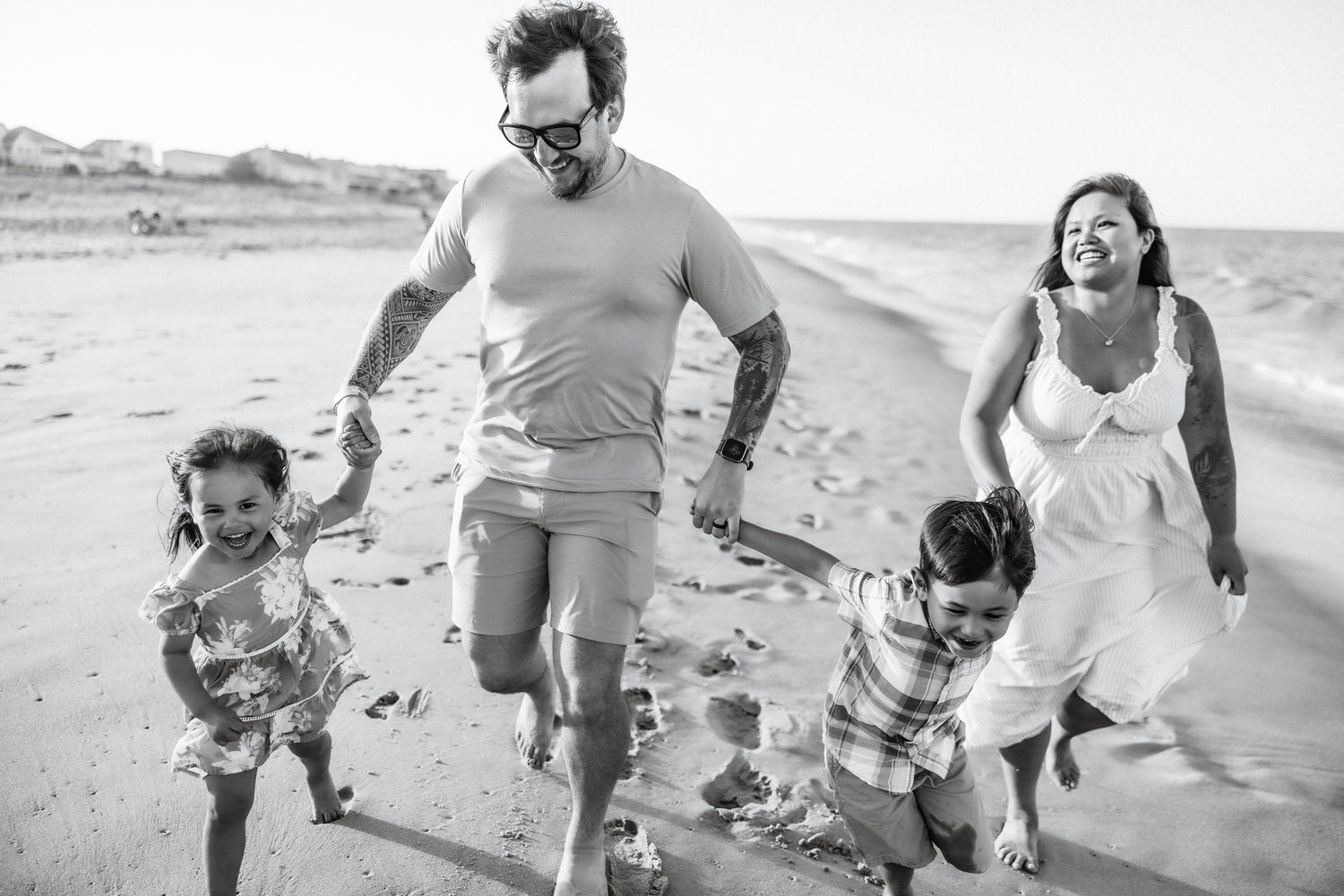 Black and white photo of a happy family running and playing together on a sandy beach near the ocean.