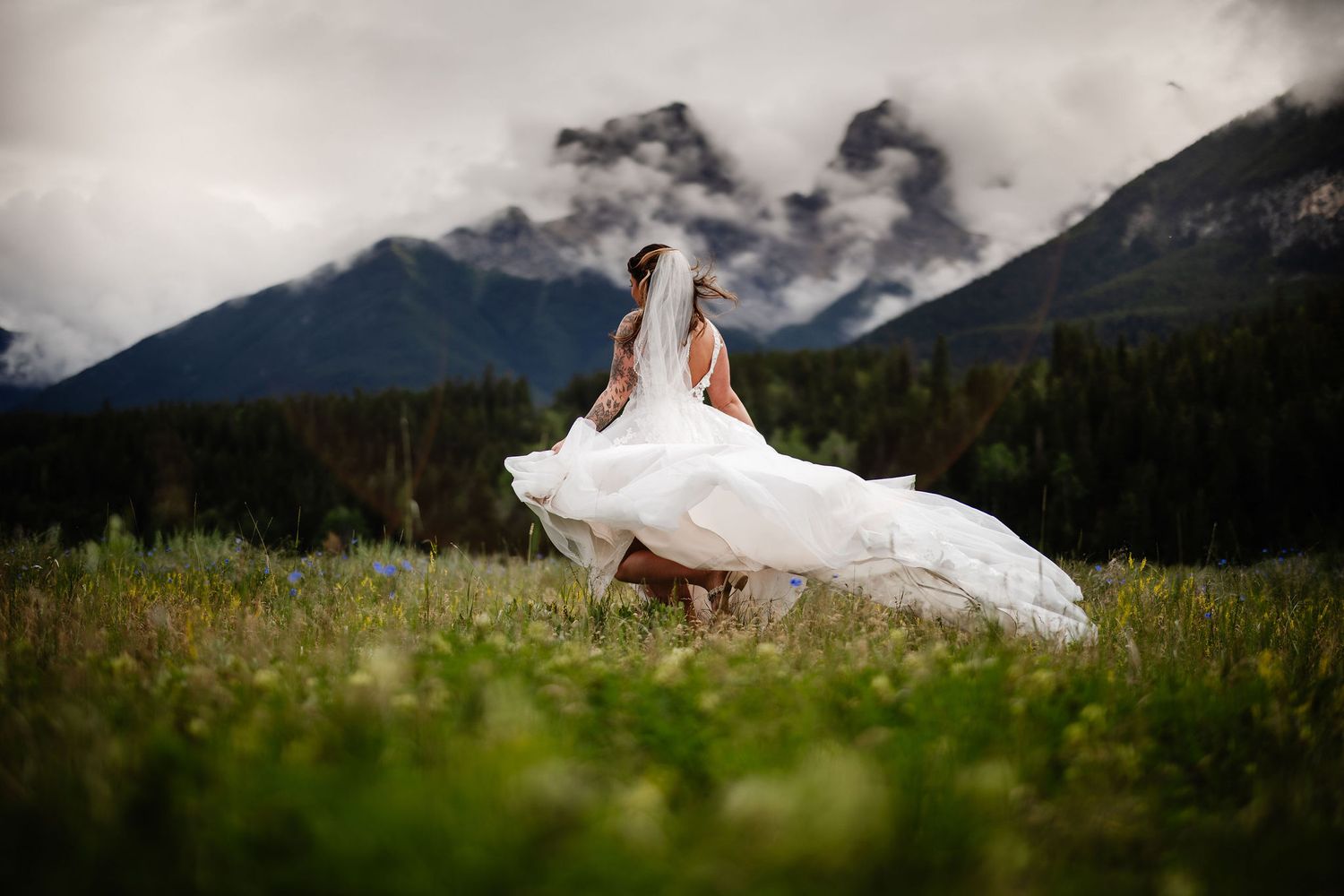 A couple shares a romantic kiss on a rocky mountain overlook with a turquoise lake and dramatic peaks in the background.