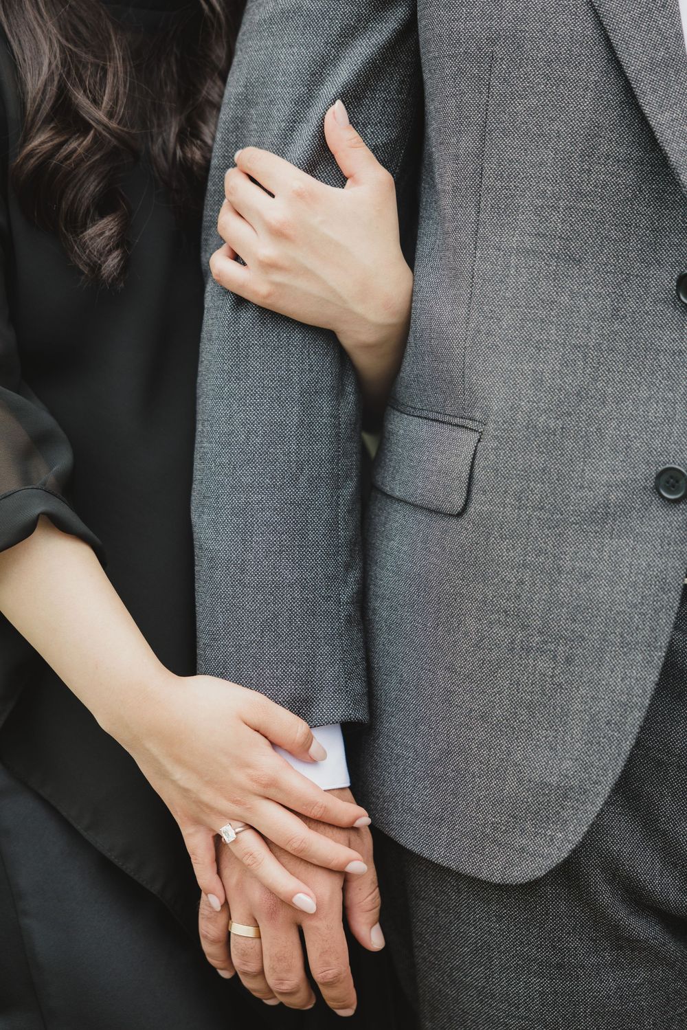 Close-up of couple holding hands, woman wearing engagement ring, man in gray suit, romantic wedding moment.