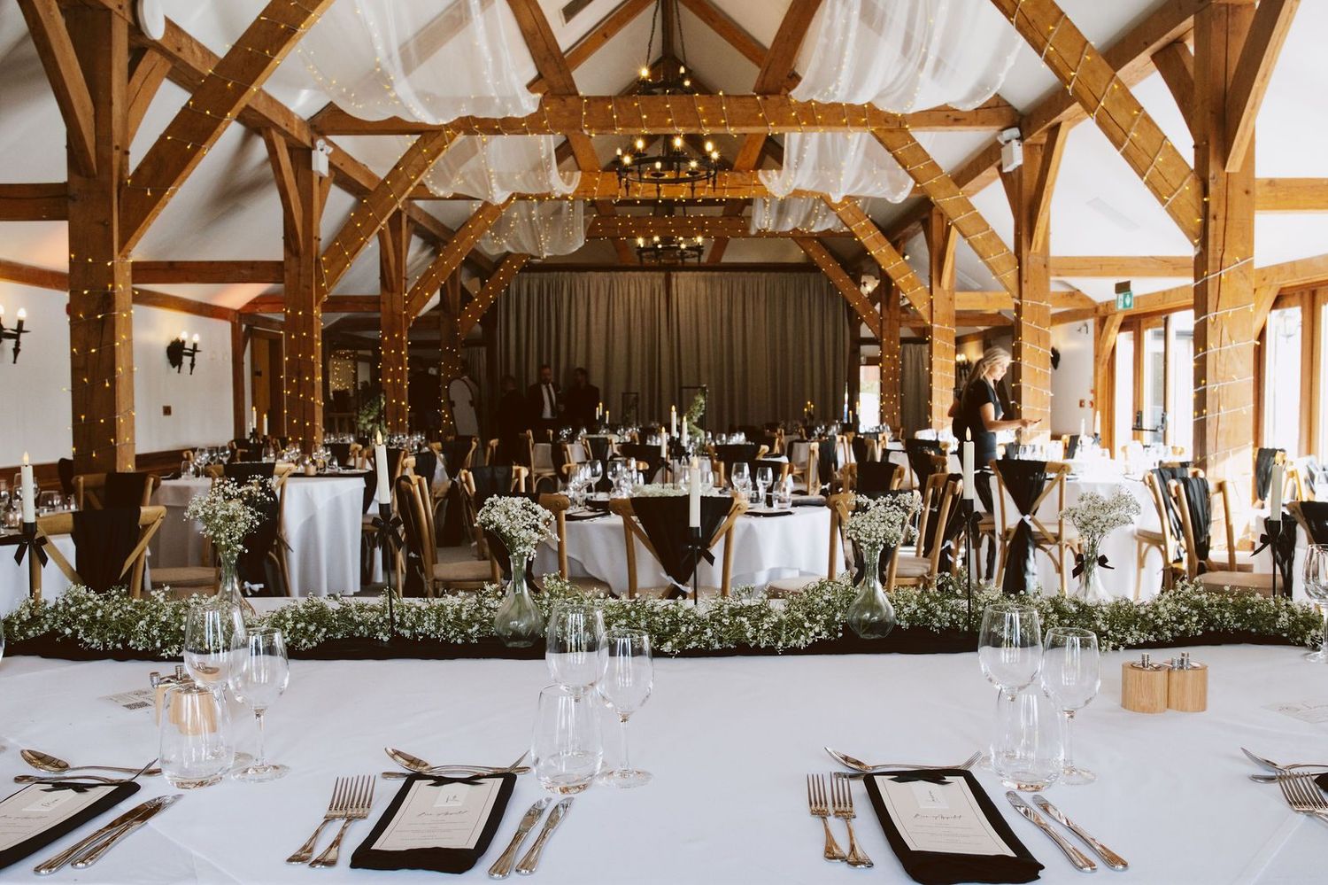 The Dining Barn at Sandhole Oak Barn set for a wedding, with oak trusses and wrought iron chandeliers