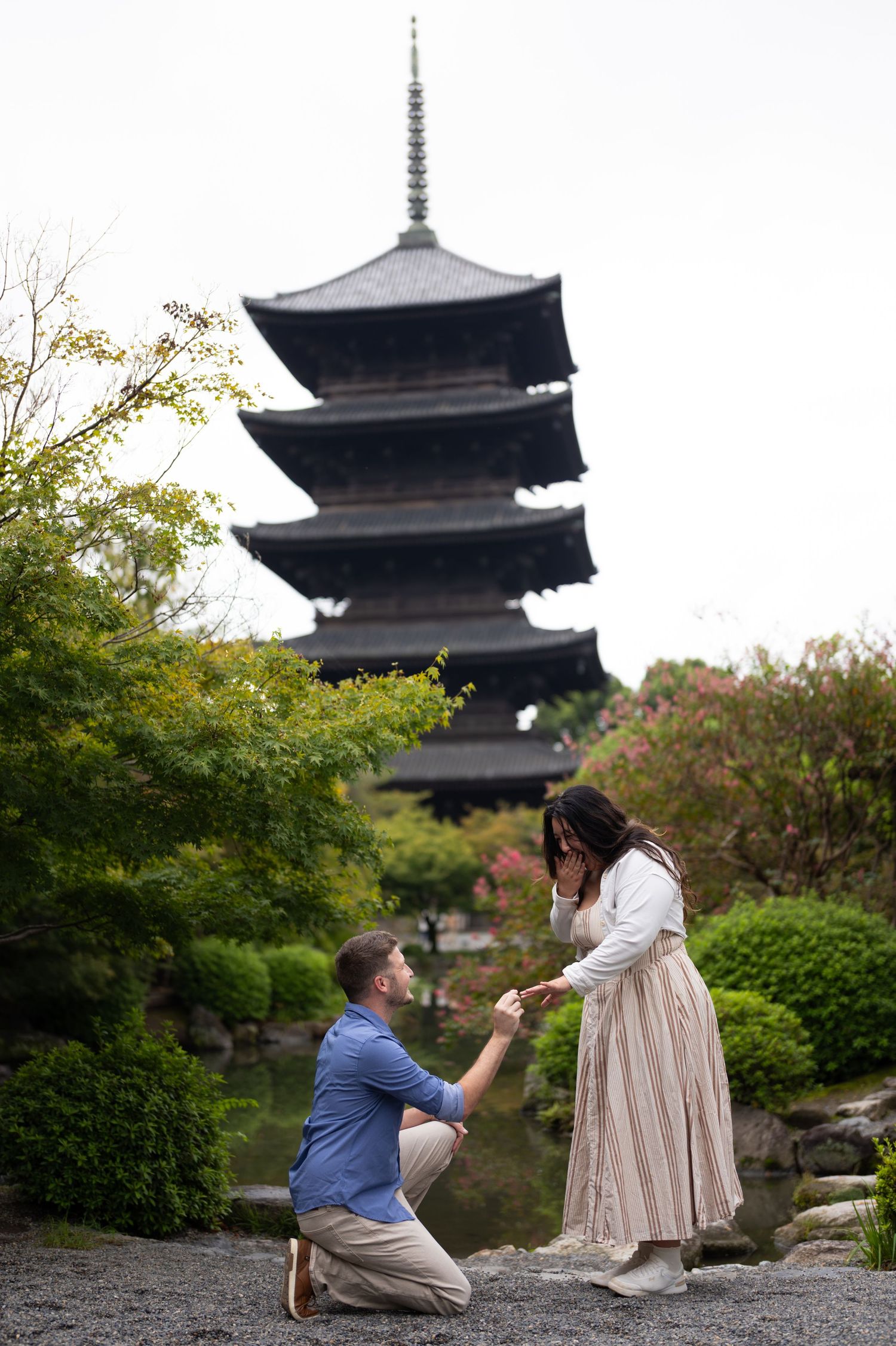 Man kneeling on one knee proposes to a woman in a garden in front of a traditional Japanese five-story pagoda.