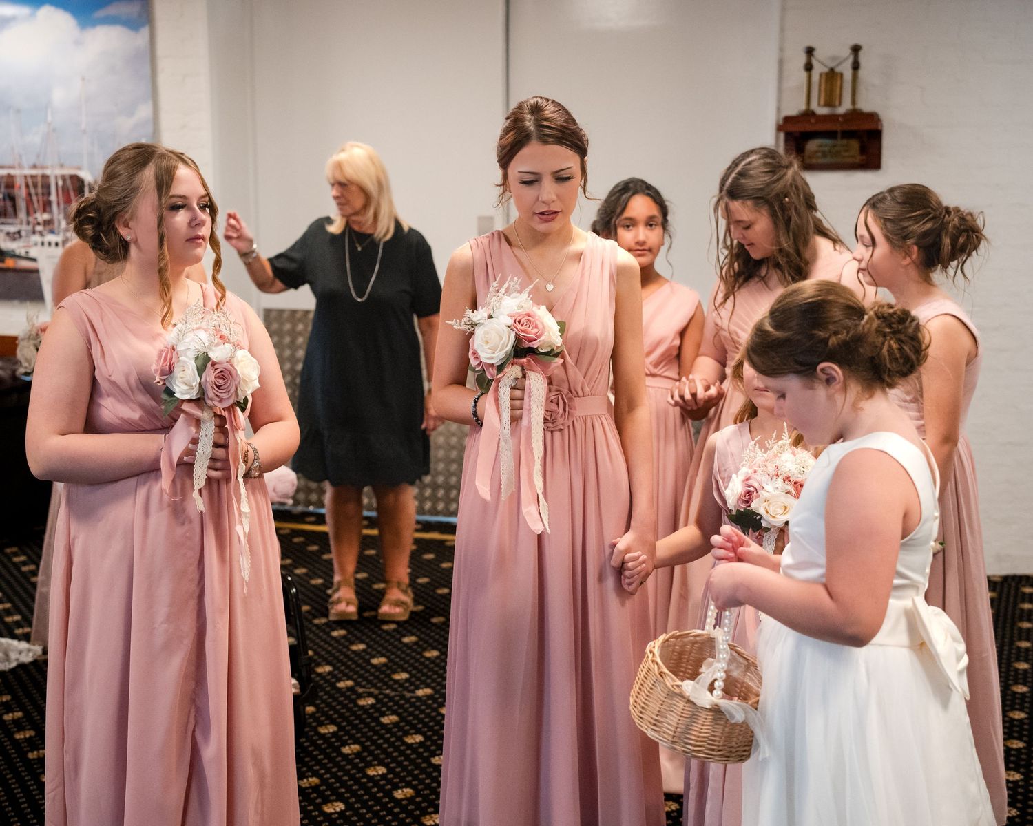Bridesmaids in blush pink gowns holding bouquets with flower girl in white dress at elegant wedding ceremony.