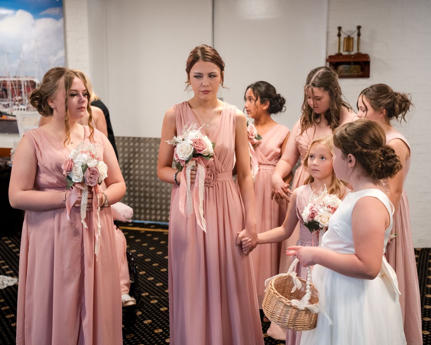 Bridesmaids in dusty pink gowns holding bouquets stand with a flower girl in white at a wedding ceremony.