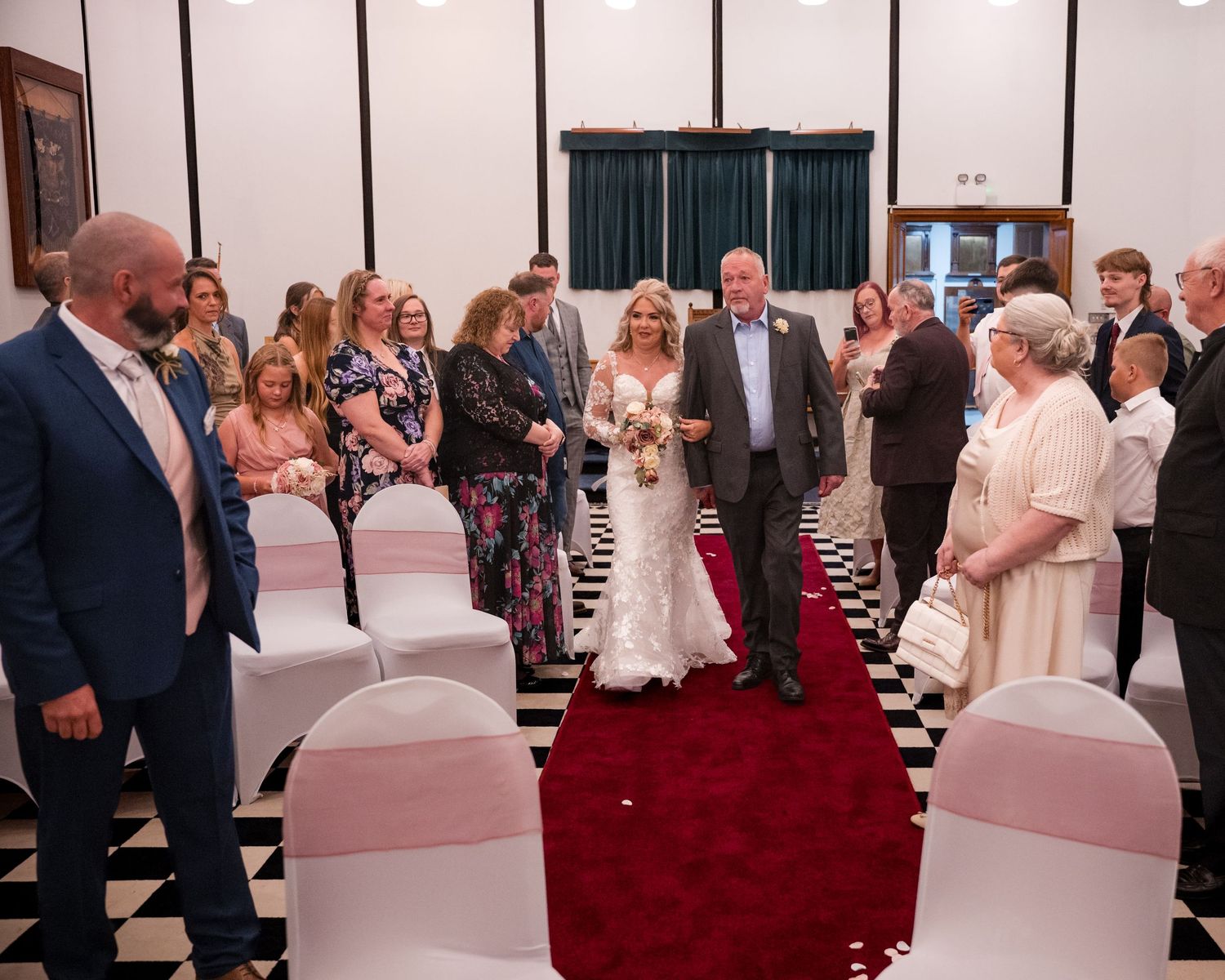 Bride walks down the aisle with escort on red carpet runner in elegant wedding ceremony venue.