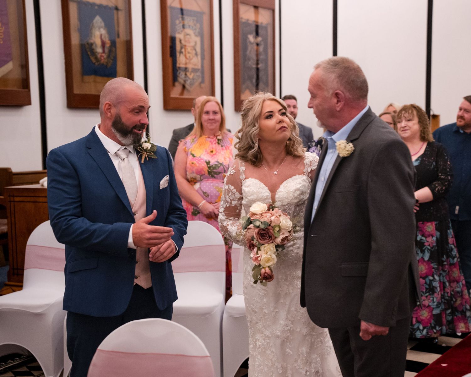 Groom greets bride and her escort at the altar during intimate wedding ceremony indoors.