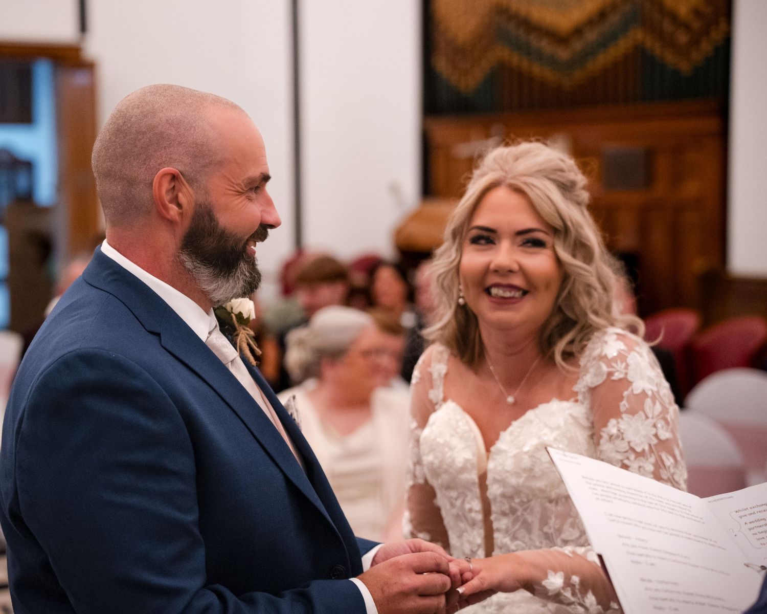 Bride and groom exchanging vows at a church wedding ceremony, bride holding vows card in lace gown.