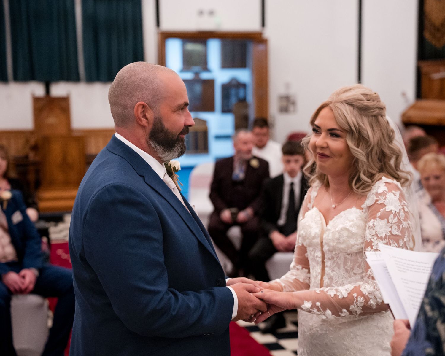 Bride and groom exchange vows holding hands at a church wedding ceremony, bride wearing lace gown.