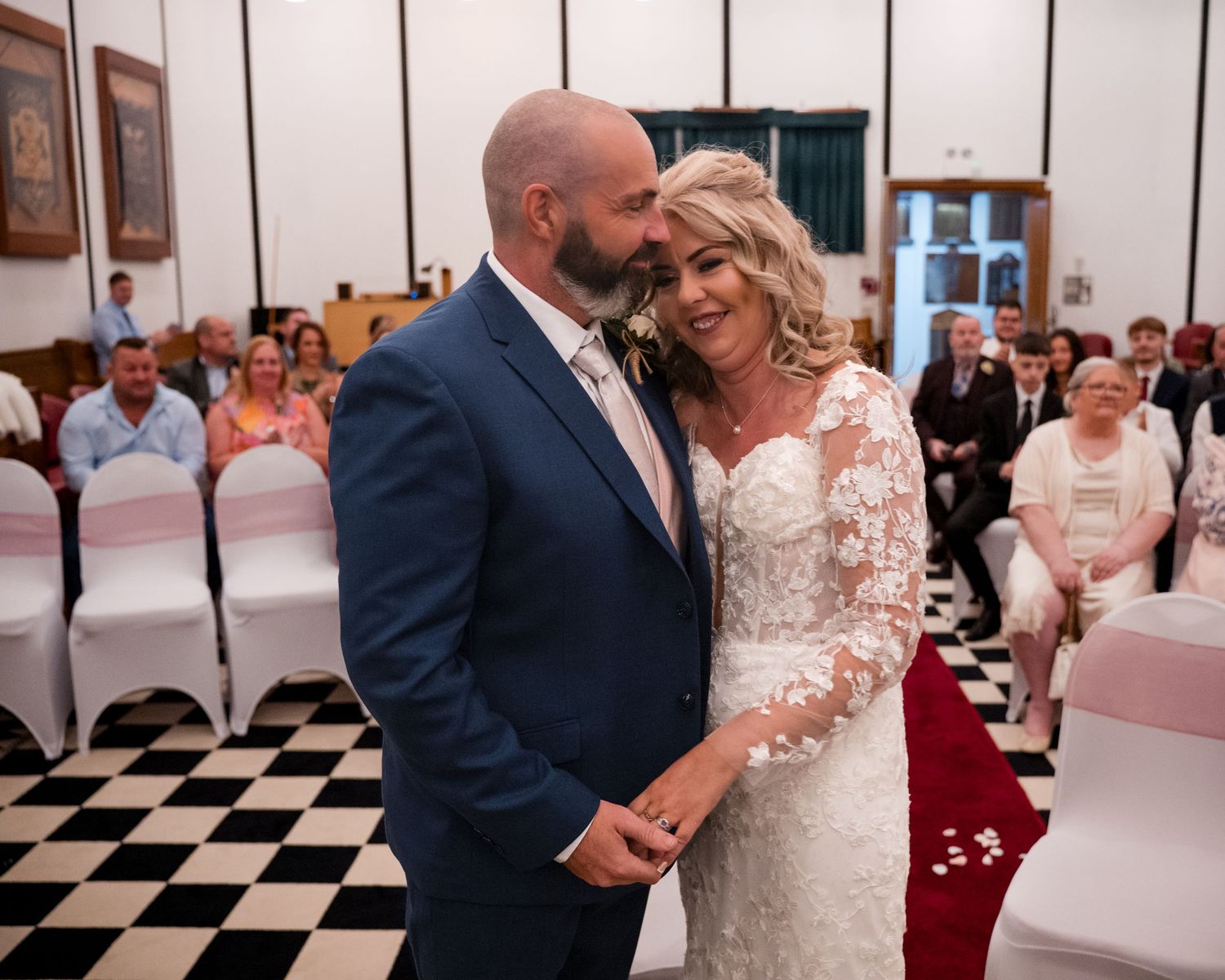Bride and groom share a romantic moment at the altar during their wedding ceremony, guests seated in rows behind them.