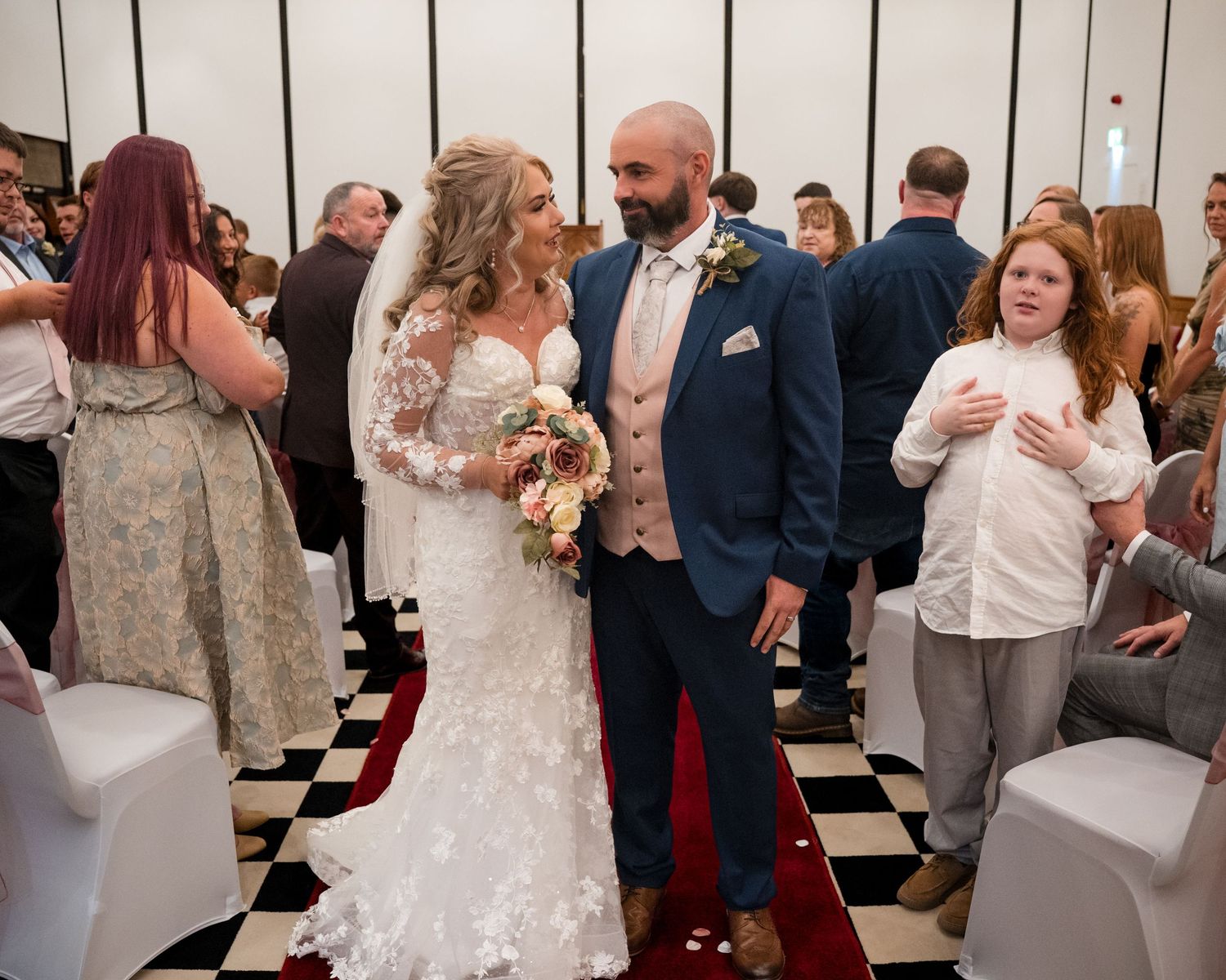 Newlywed couple sharing a joyful moment walking down the aisle at their wedding ceremony on a checkered floor.