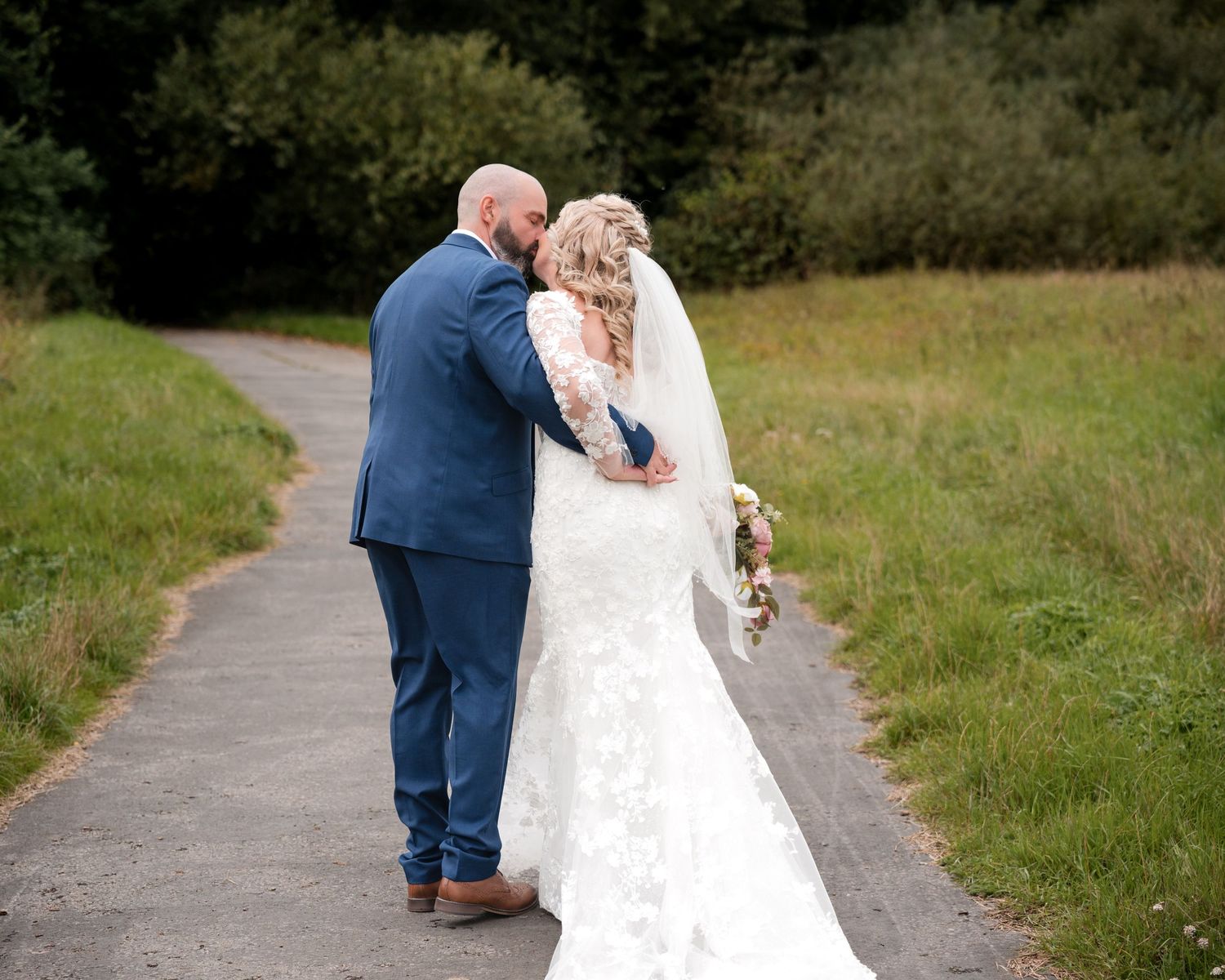 A bride and groom walk hand in hand down a path surrounded by lush greenery on their wedding day.