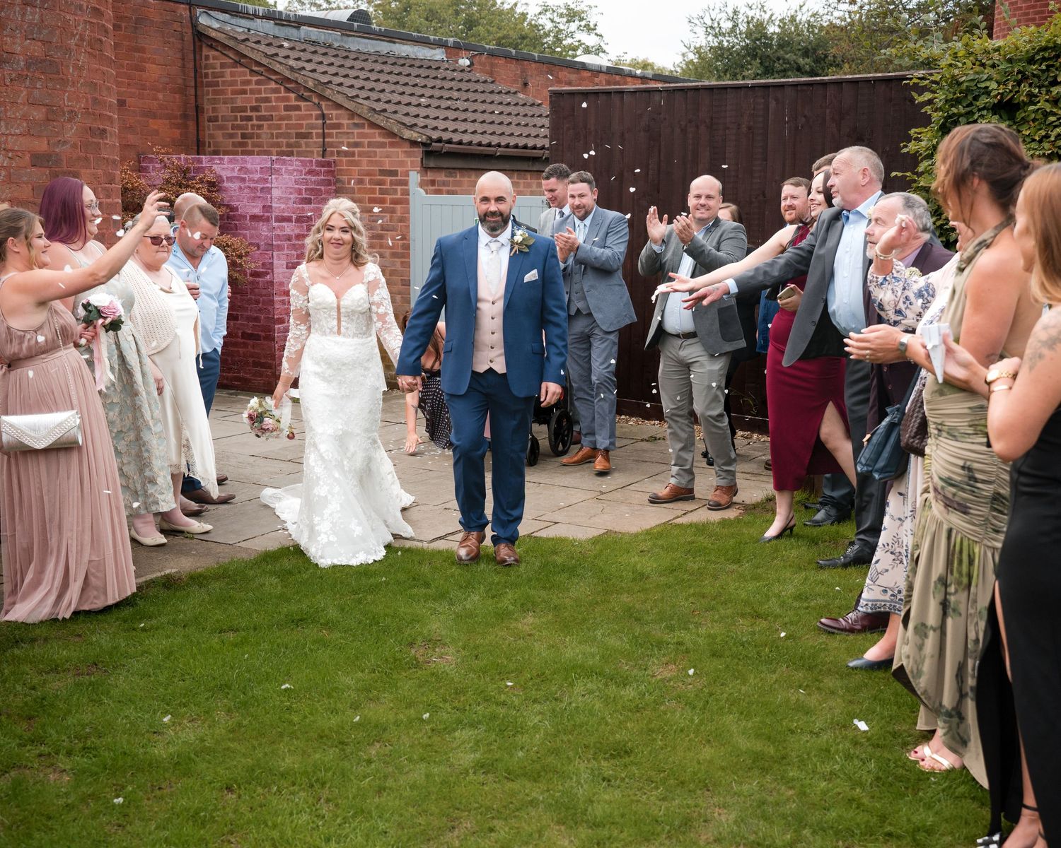 Bride and groom walk through cheering guests in sunny garden wedding ceremony celebration.