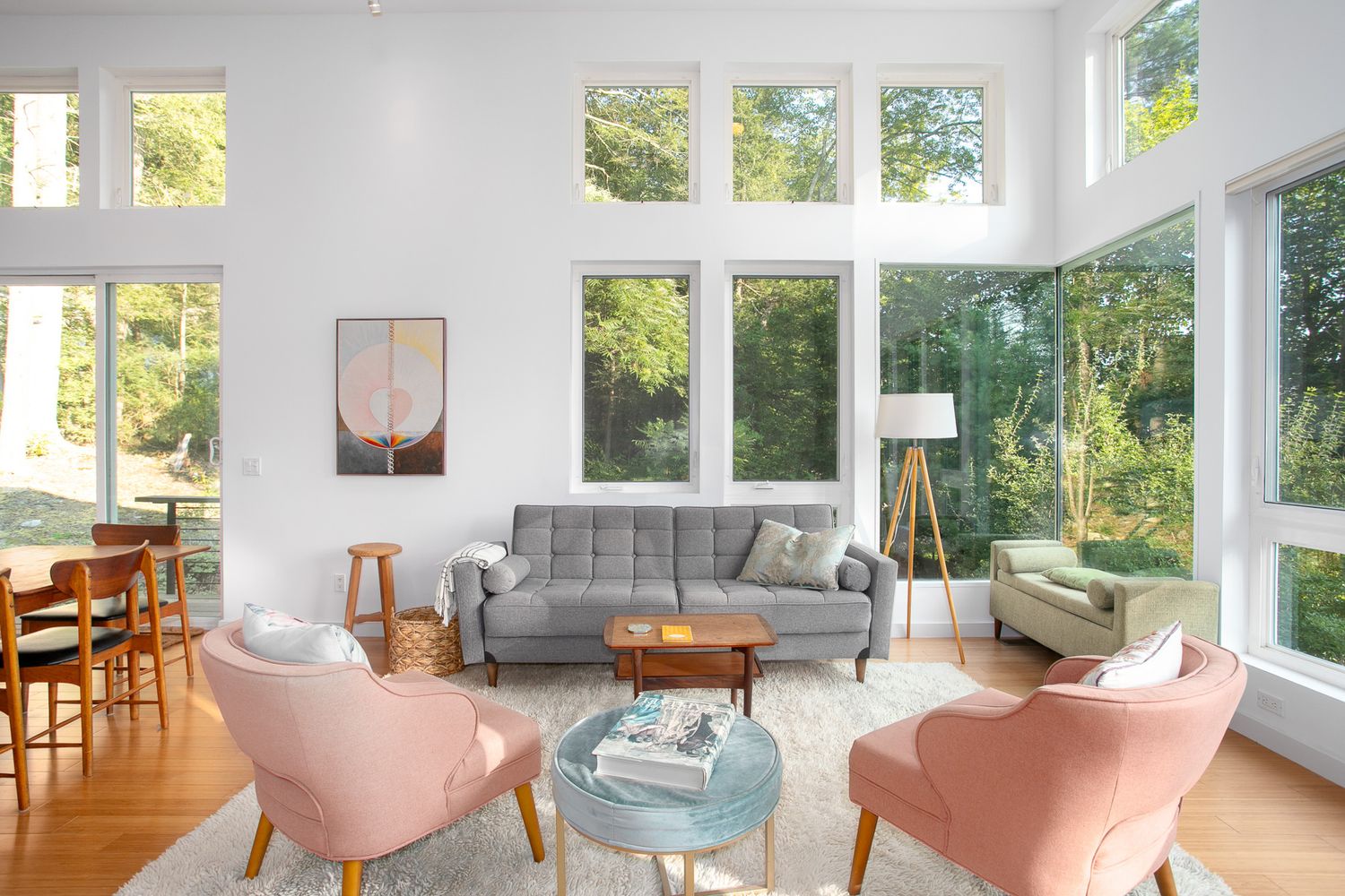 Bright modern living room with high ceilings, large windows, gray sofa, and pink accent chairs.