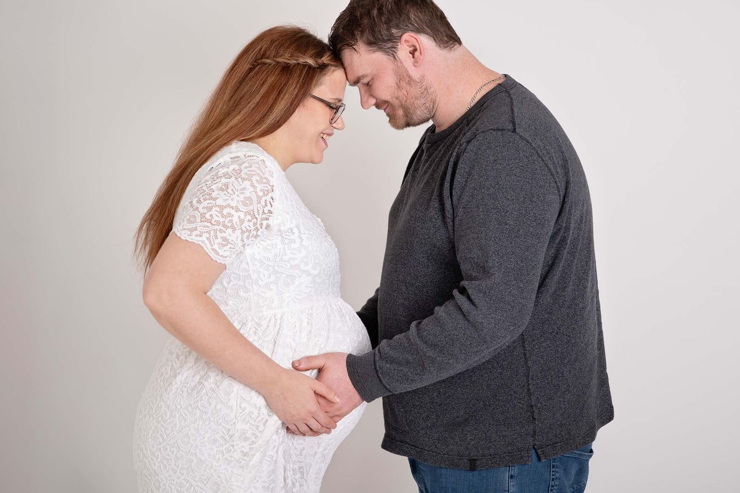 Maternity session of expecting mother stand facing husband with their hands on her belly for studio session in Baltimore Ontario.