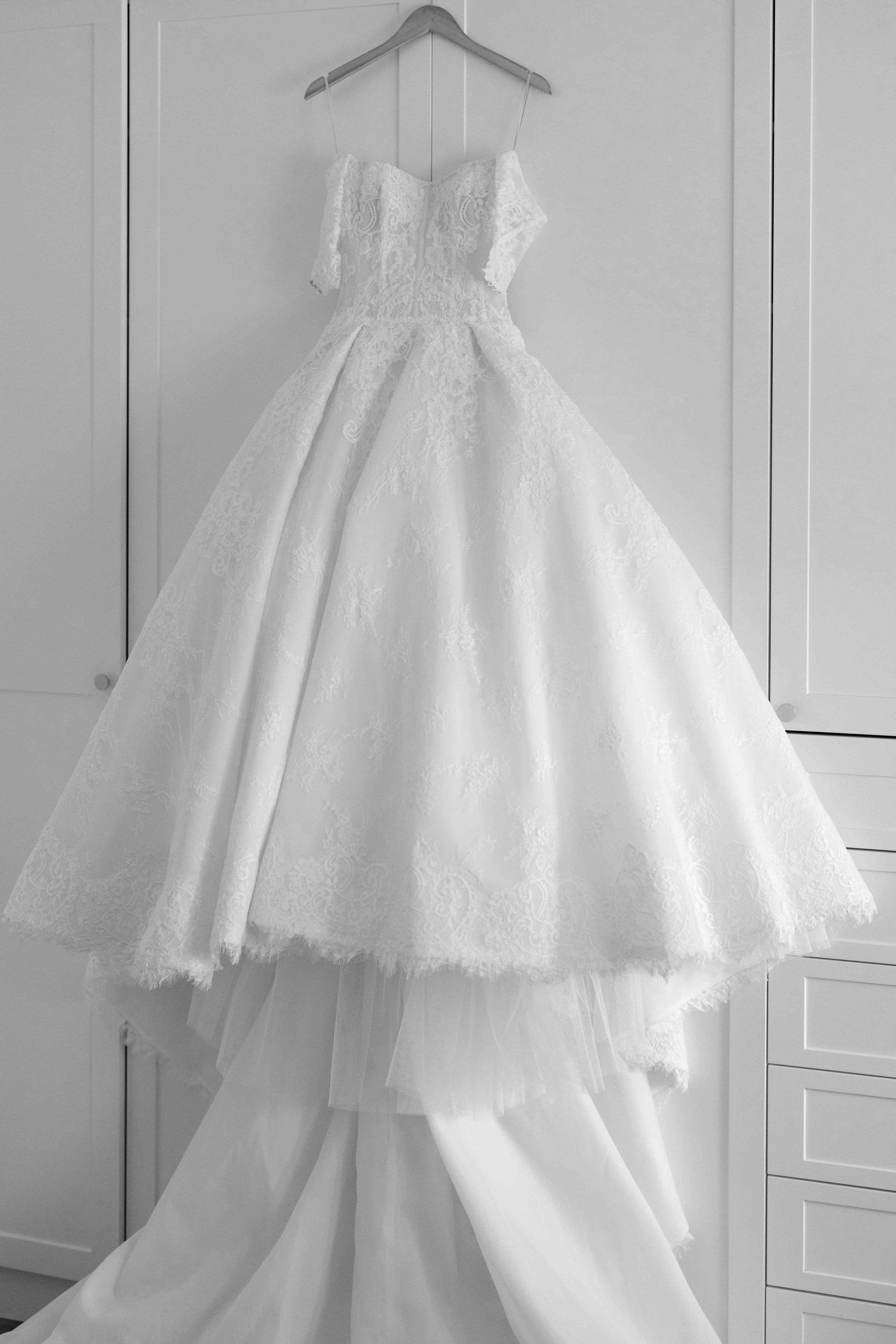 Elegant white ball gown wedding dress with lace bodice and tiered skirt hanging on a hanger.