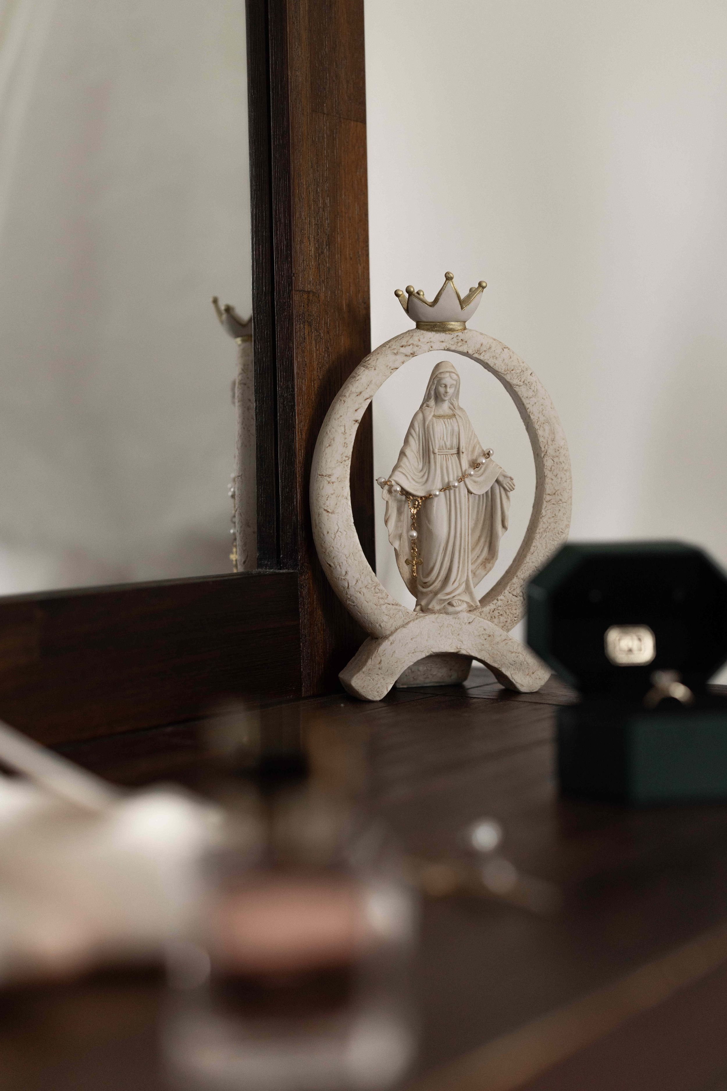 White ceramic Virgin Mary figurine with gold crown on wooden dresser beside mirror.