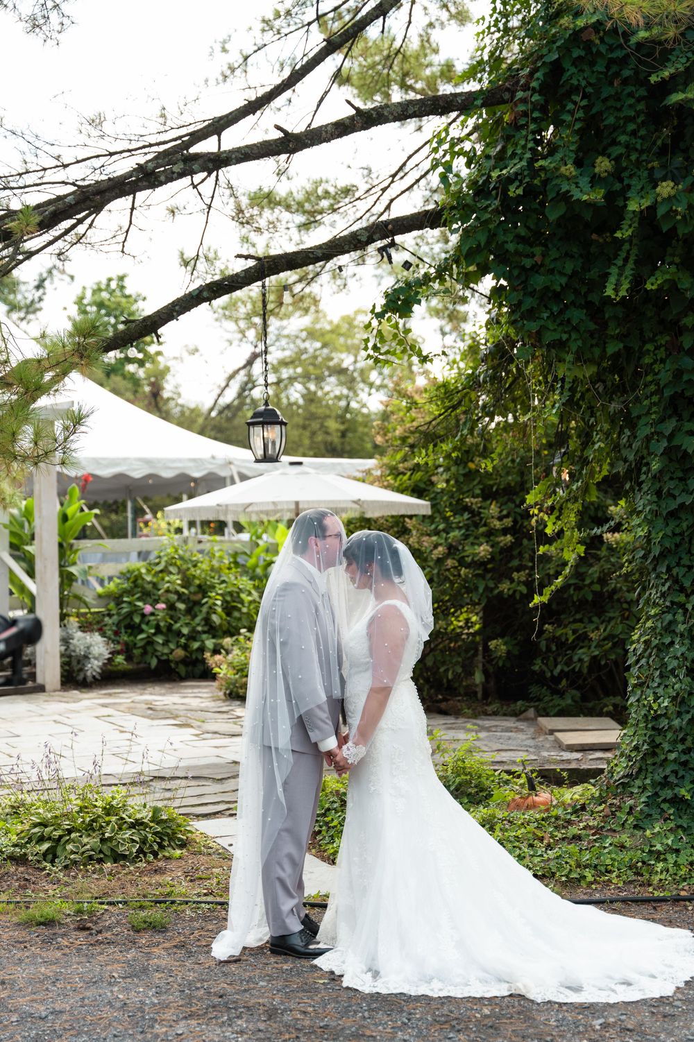 Bride and groom share a romantic kiss outdoors, surrounded by lush greenery and ivy-covered walls at their wedding venue.
