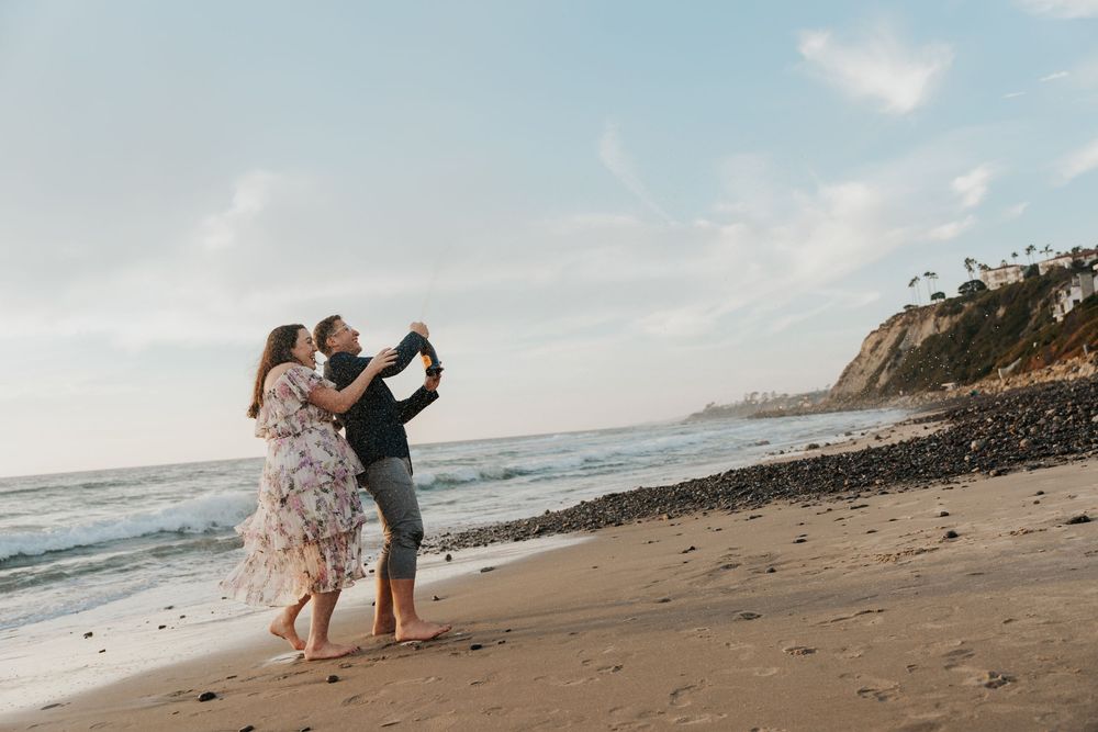 Couple sharing a romantic kiss on a sandy beach at sunset with ocean waves and cliffs in the background.