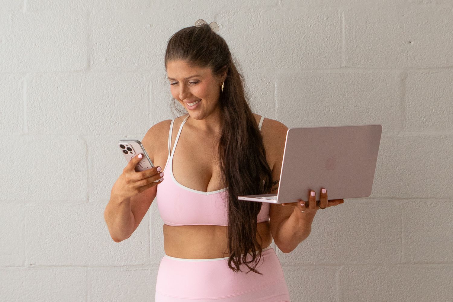 Woman in beige top and pink shorts rolling up a pink yoga mat on a gray floor.