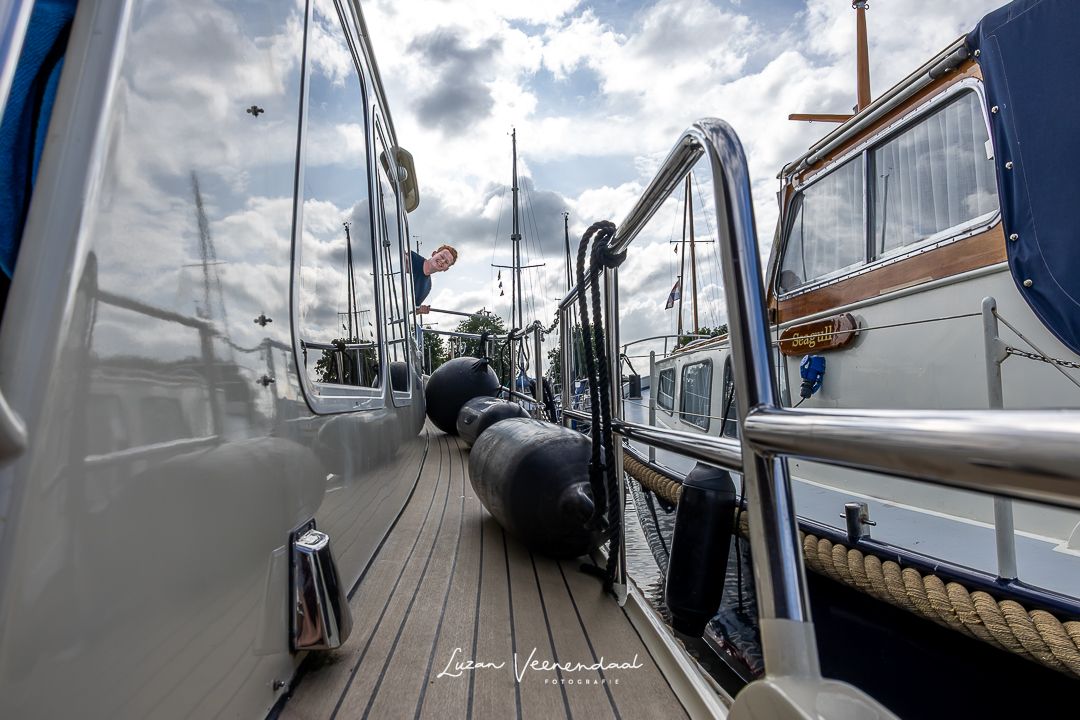 Zoon kijkt om het hoekje van de boot terwijl deze nog in de haven van Uitgeest ligt