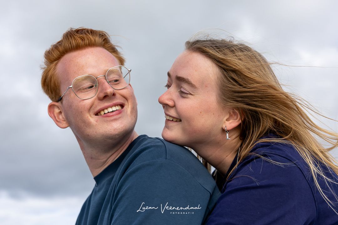 Vriendin zit achter haar vriend met haar haar in de wind, hij kijkt om naar haar tijdens de familiefotoshoot op de boot in Uitgeest