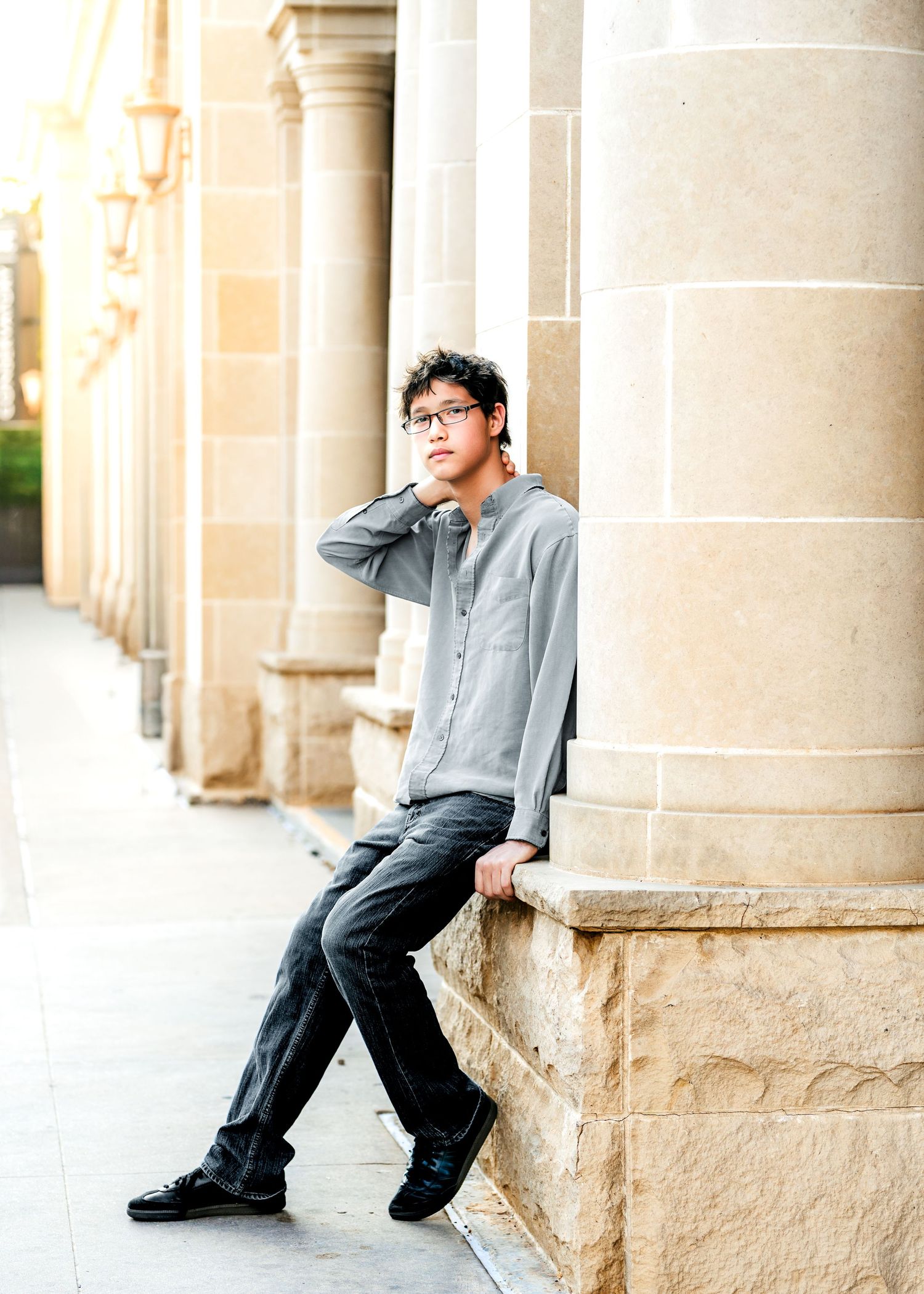 Young man in glasses and gray shirt leaning against stone column at a classic building.