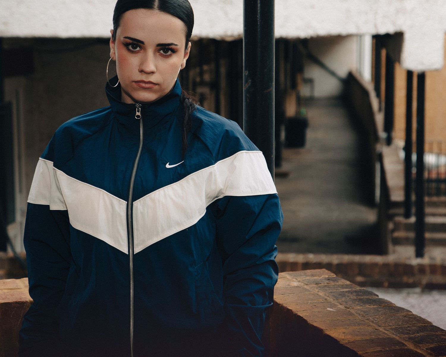 Young woman in navy blue and white Nike windbreaker jacket posing outdoors in an urban setting.