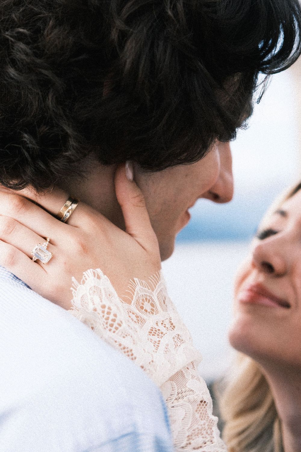 Close-up of a woman wearing a diamond engagement ring and lace sleeve embracing a man tenderly.