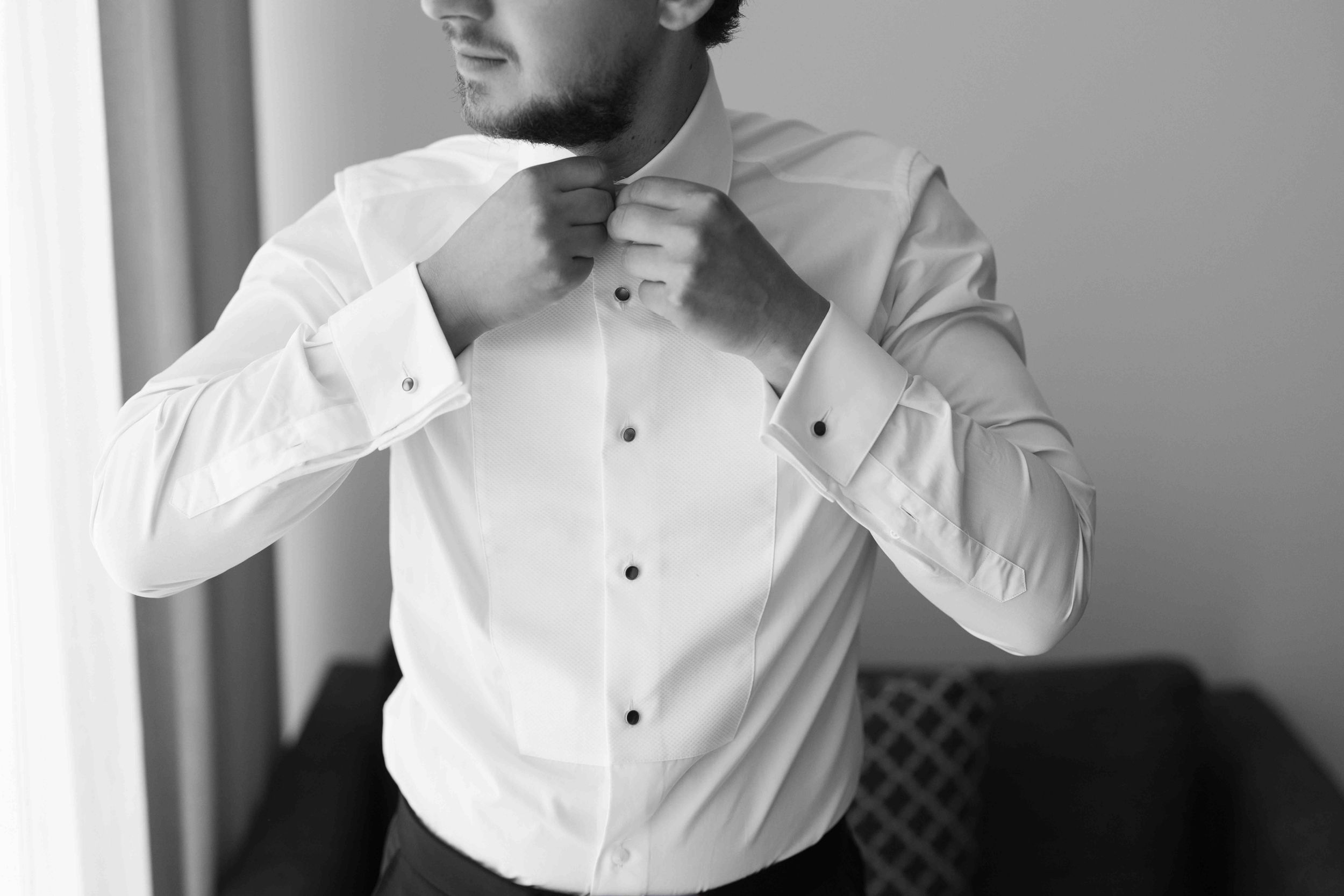 Man in white dress shirt adjusting collar buttons, black and white professional photo.