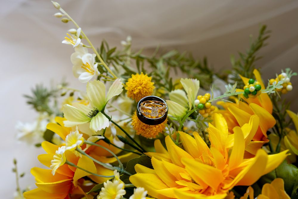 Gold wedding rings rest on a vibrant bouquet of yellow sunflowers and white daisies for a wedding ceremony.