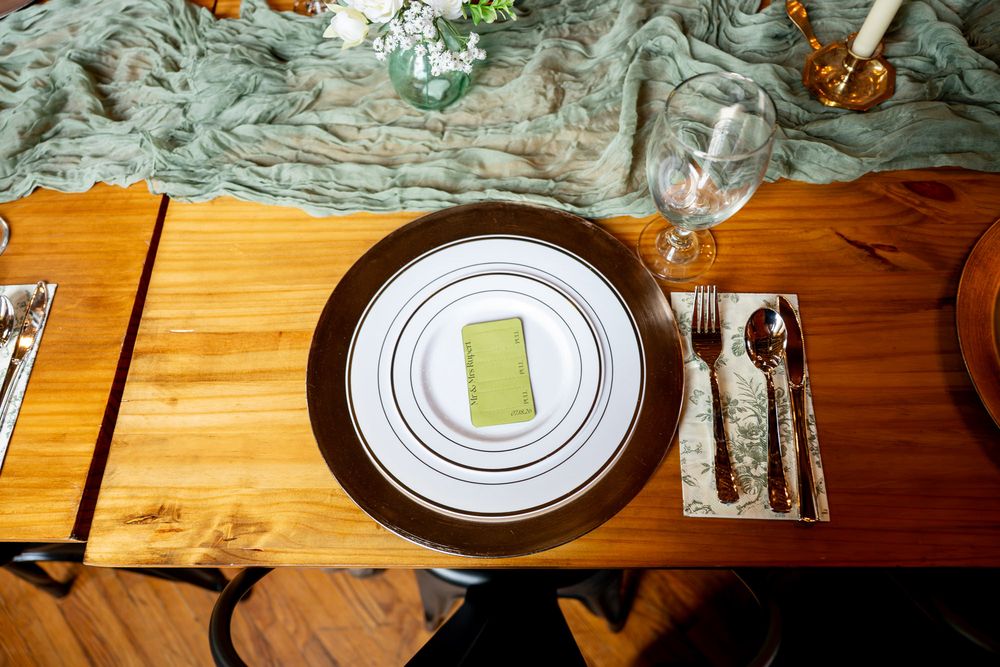 Elegant table setting with green napkin, white plate, gold charger, silverware, and wine glass on wooden table.