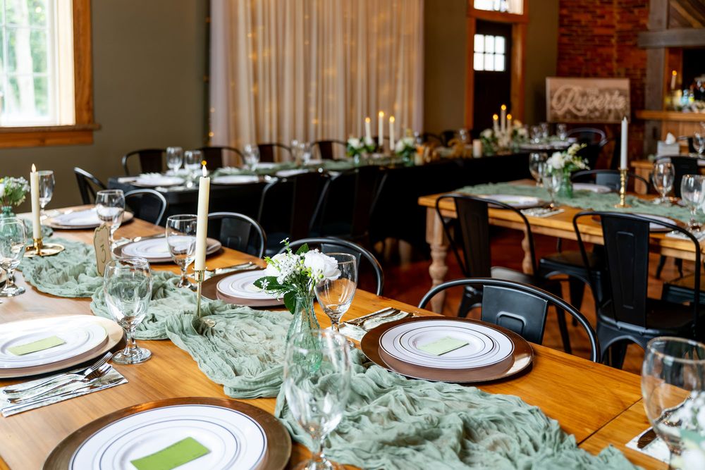 Elegant wedding reception tables with greenery runners, white plates, candles, and wine glasses in a rustic venue.
