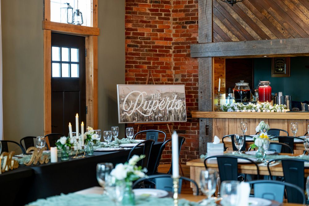 Rustic wedding reception venue with brick walls, wooden decor, elegant table settings, candles, and a decorative Rupert's sign.