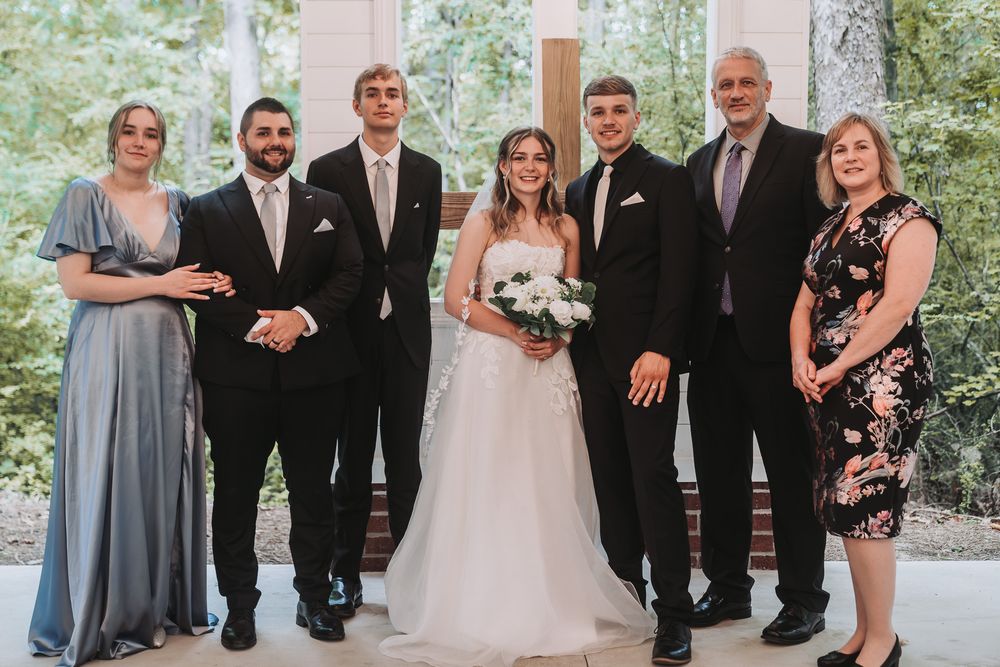 Wedding party posing together in a chapel, bride in white gown holding bouquet with family in formal attire.