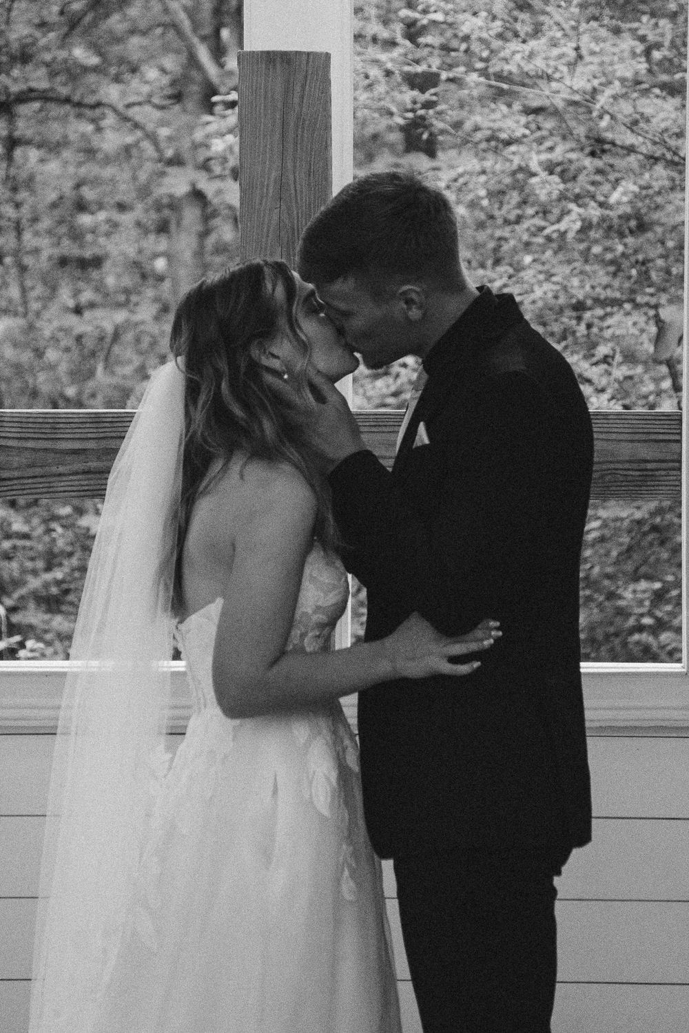 Black and white photo of a bride and groom sharing an intimate moment, nearly kissing at an outdoor wedding ceremony.