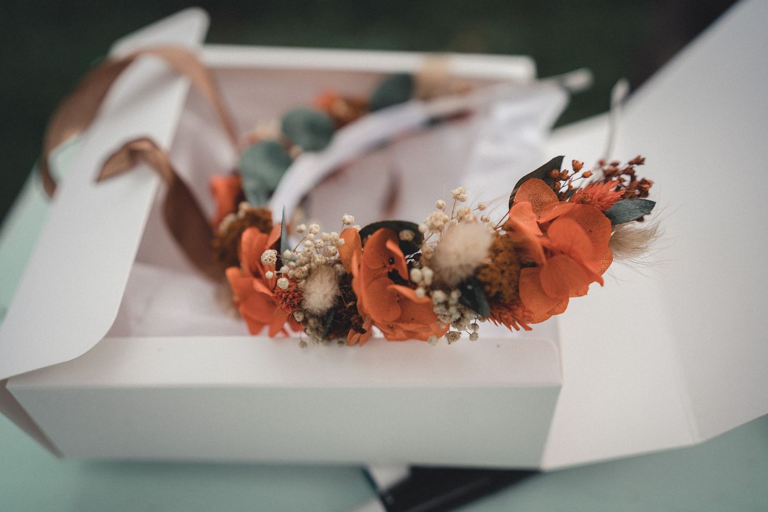 An elegant dried floral hair crown with orange blooms displayed in a white gift box.