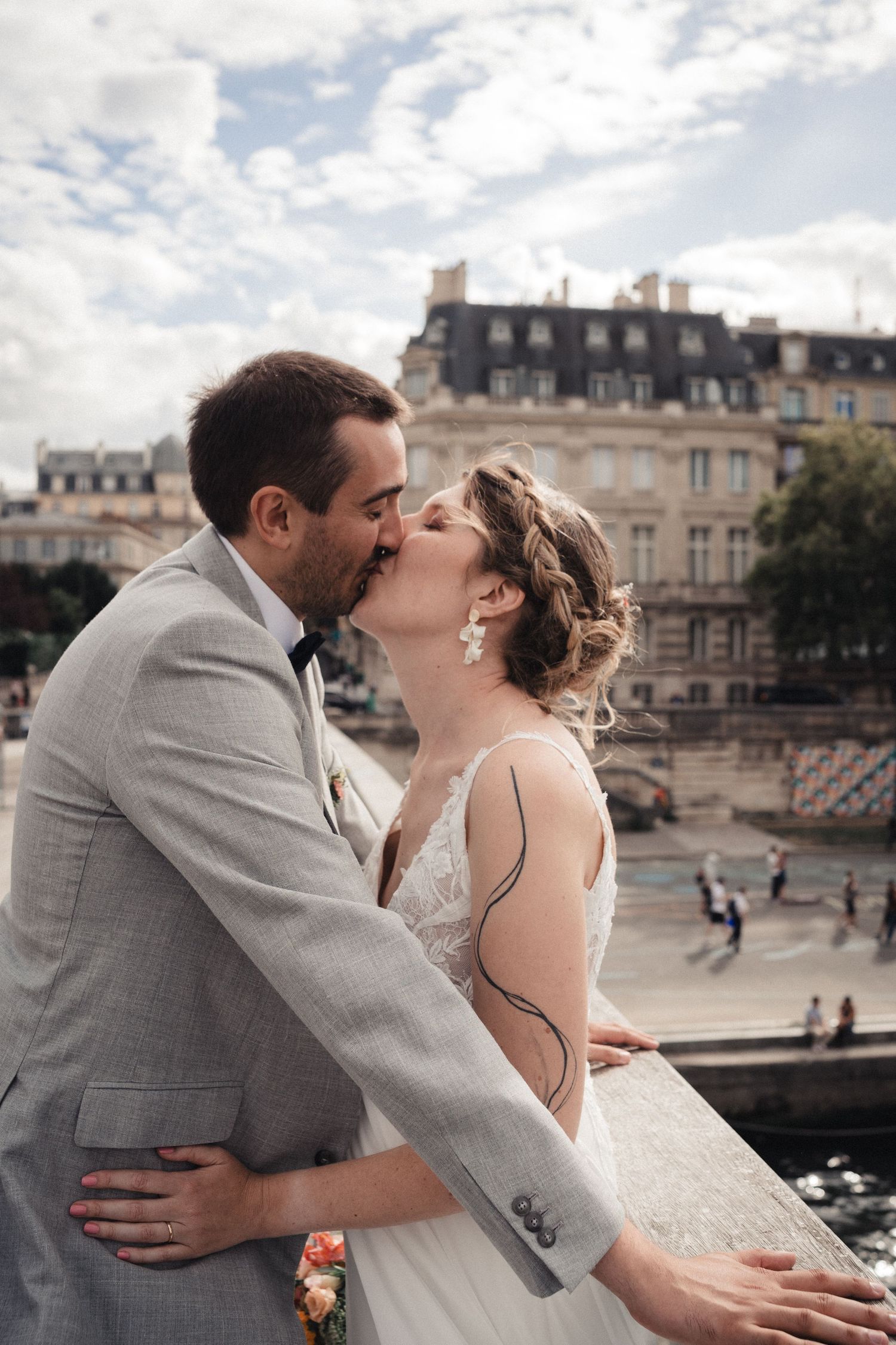 Bride and groom share a romantic kiss in Paris, with classic Haussmann buildings and the Seine River in the background.