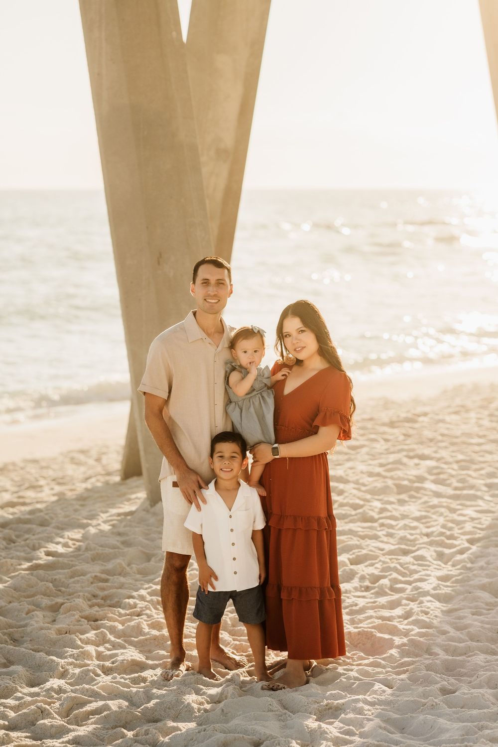 Family of four posing together beneath the pier on Pensacola Beach at golden hour