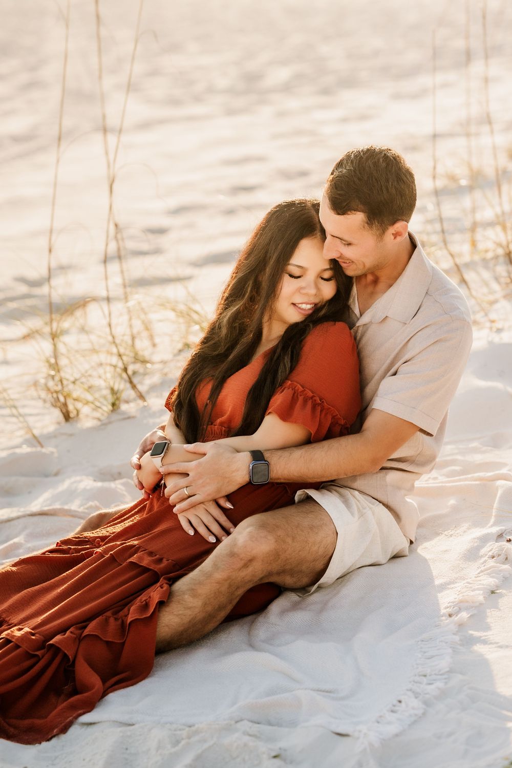 Couple cuddling together in the sand during a golden hour beach session