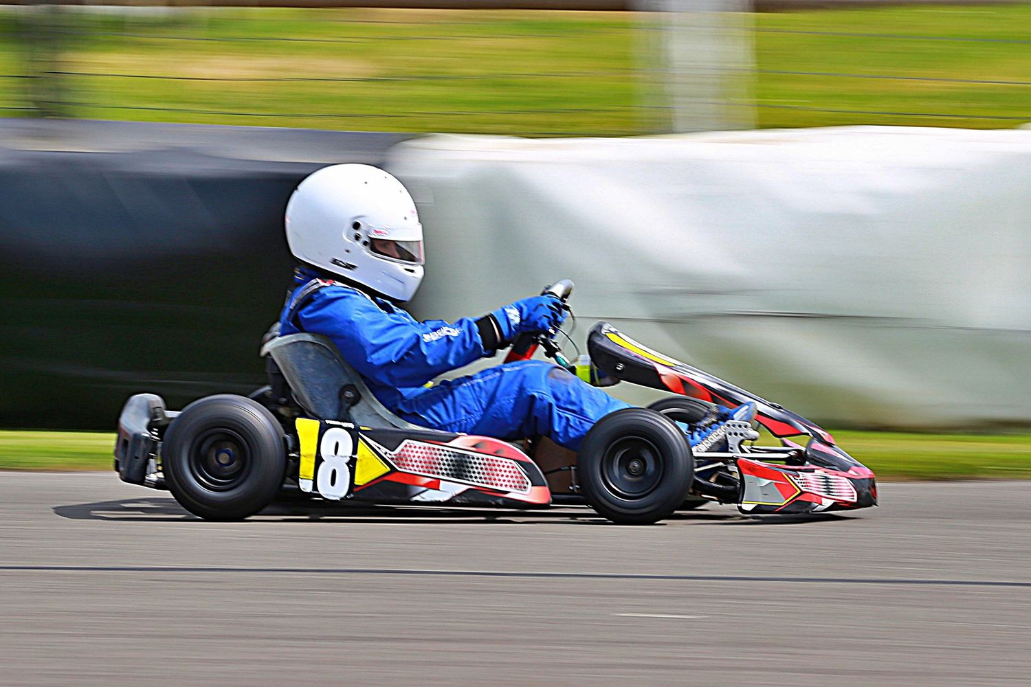 Go-kart racer number 18 in blue racing suit navigating a corner on an outdoor karting circuit.