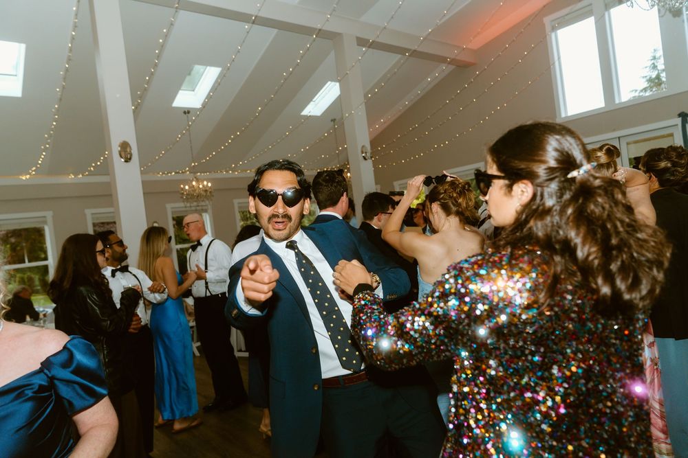 Guests dancing and celebrating at a wedding reception in a decorated venue with string lights.