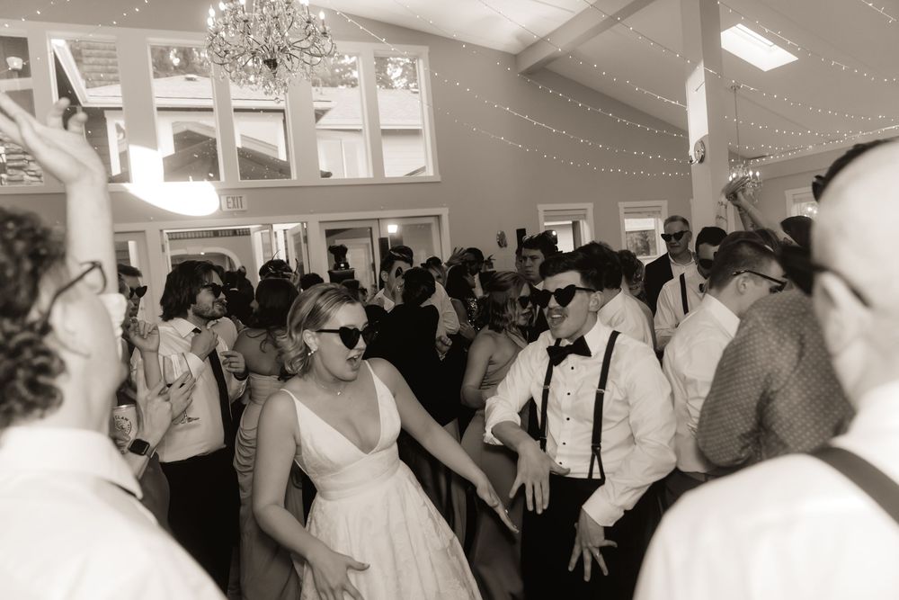 Bride and groom dancing with guests at a lively wedding reception in black and white photo.