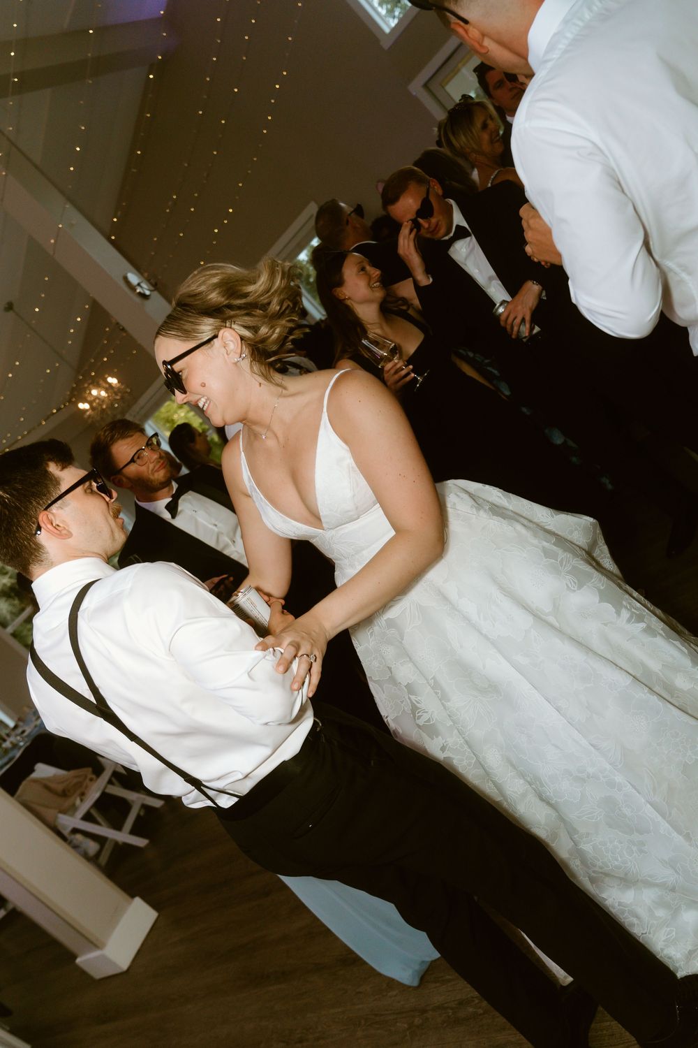 Bride and groom share their first dance at wedding reception, smiling joyfully in elegant white gown and suspenders.